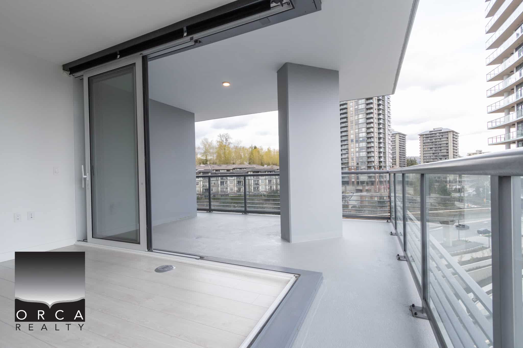 Spacious balcony with glass railing and city view in modern condo, ideal for relaxing or entertaining in Vancouver, BC. Perfect for those seeking luxury real estate in a high-rise community.