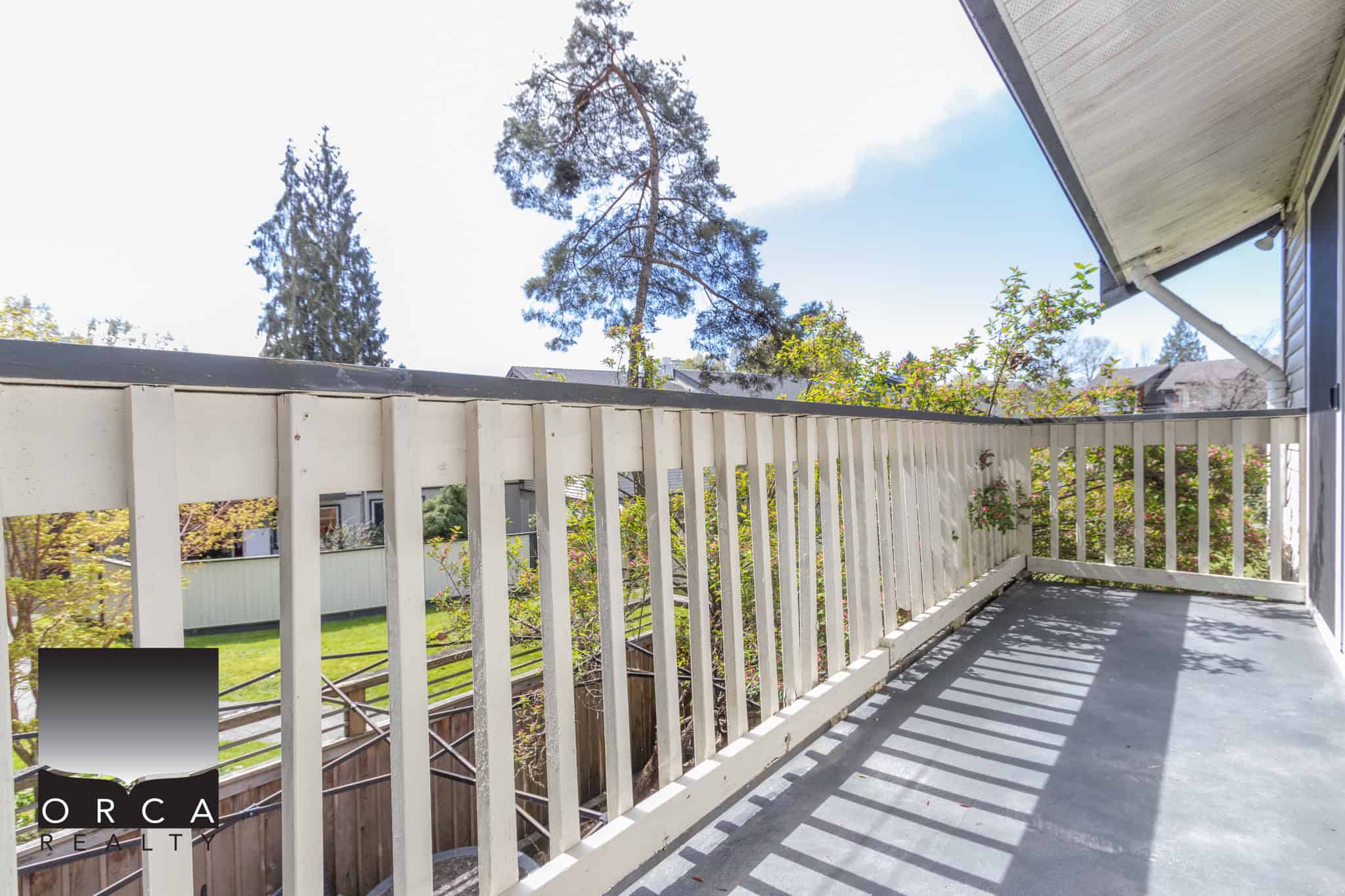 Spacious balcony with white wooden railing and view of lush greenery and tall trees, ideal for outdoor living; features in Vancouver real estate listings.