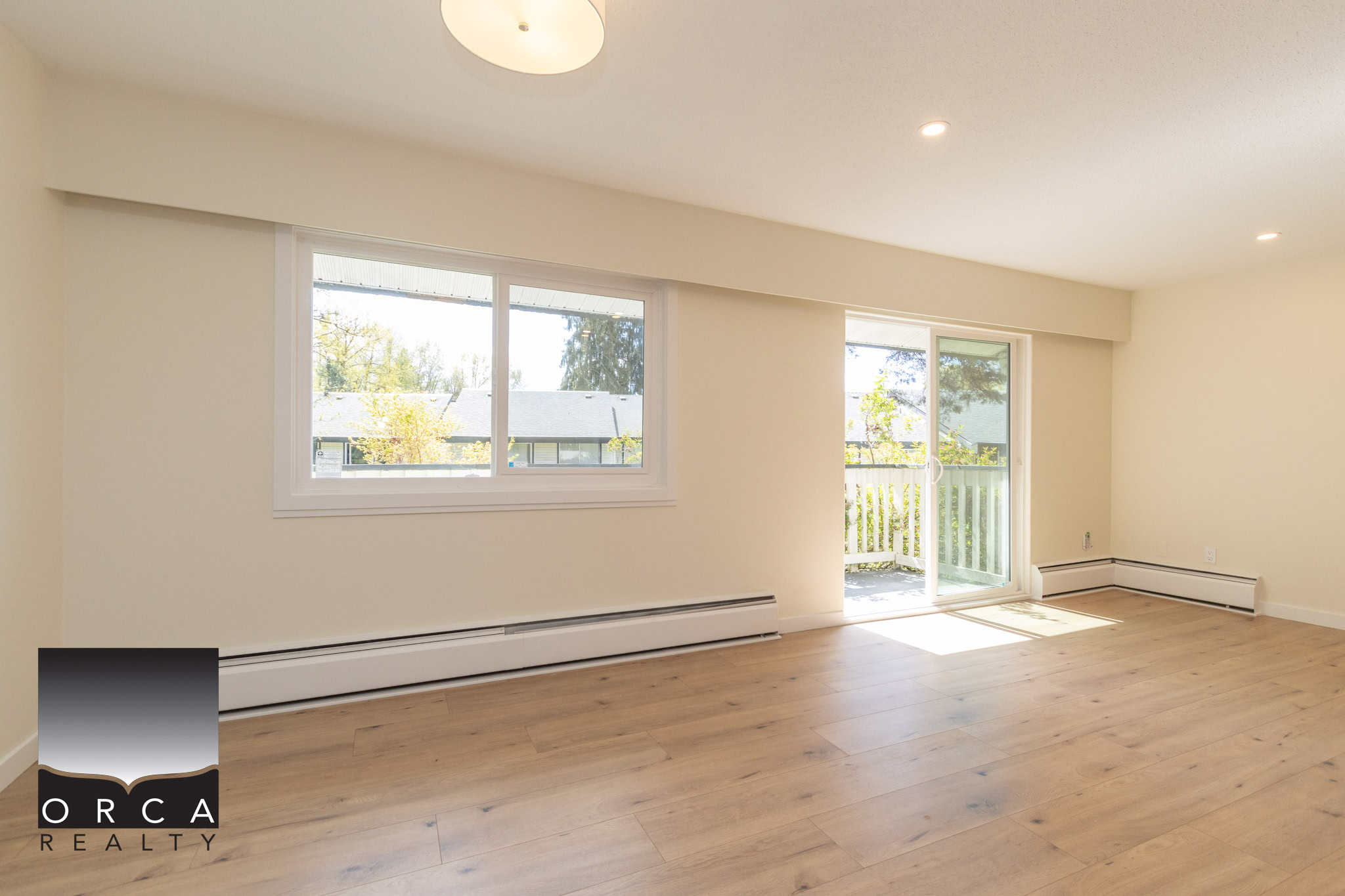 Bright living room with spacious windows and sliding glass door leading to a balcony, featuring natural light and hardwood floors, ideal for Vancouver area homes marketed by Orca Realty Inc.
