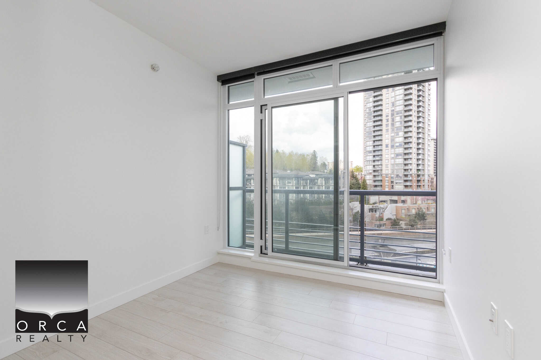 Bright modern condo interior with large glass sliding doors leading to a balcony, city view, minimalist design, light wood flooring, ideal for Vancouver real estate listings.