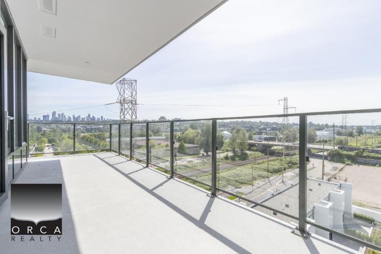 Spacious balcony with glass railing overlooking city skyline and lush greenery, ideal for Vancouver real estate enthusiasts and outdoor living.