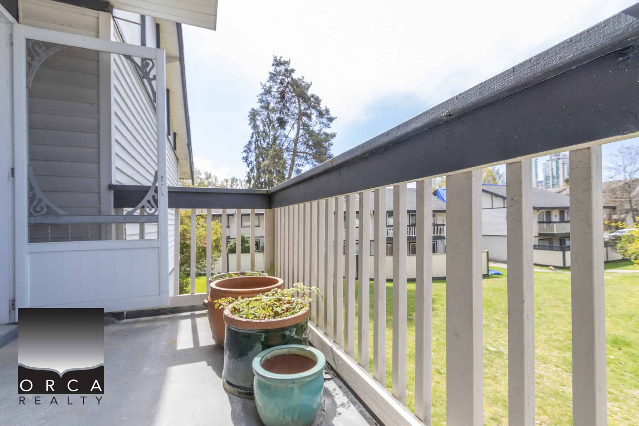 Balcony view of a condo in a residential complex, with potted plants and a surrounding grassy area, showcasing the outdoor space and community environment in Victoria, BC.