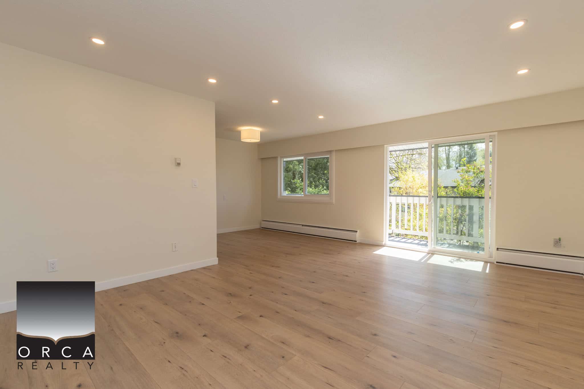 Bright and spacious living area with large windows and sliding glass door, showcasing a modern, well-lit apartment for sale or rent by Orca Realty Inc. in Vancouver, BC.
