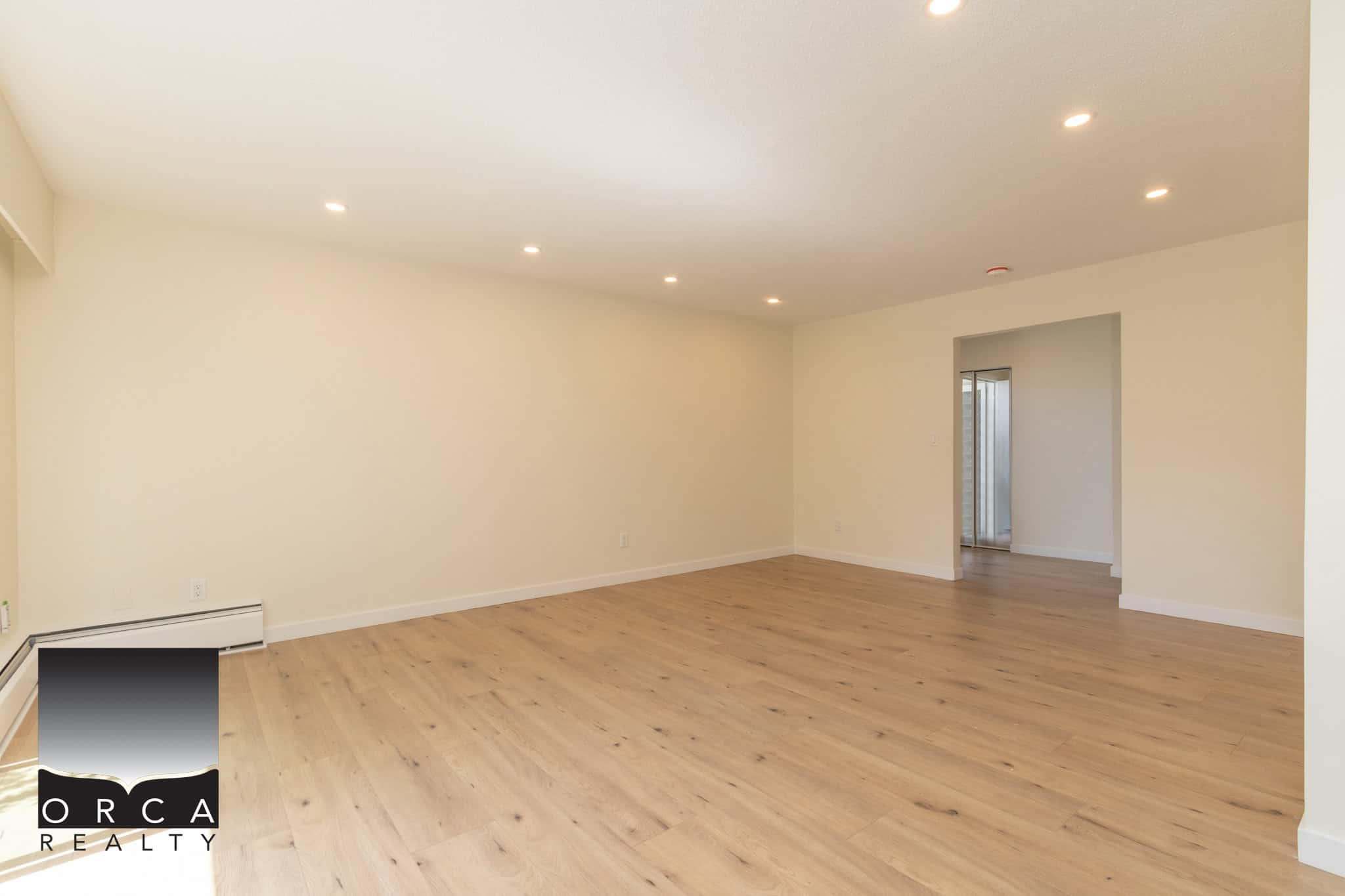 Bright, spacious empty living room with hardwood floors, neutral walls, recessed lighting, and open layout, ideal for home staging and real estate marketing in Victoria BC.