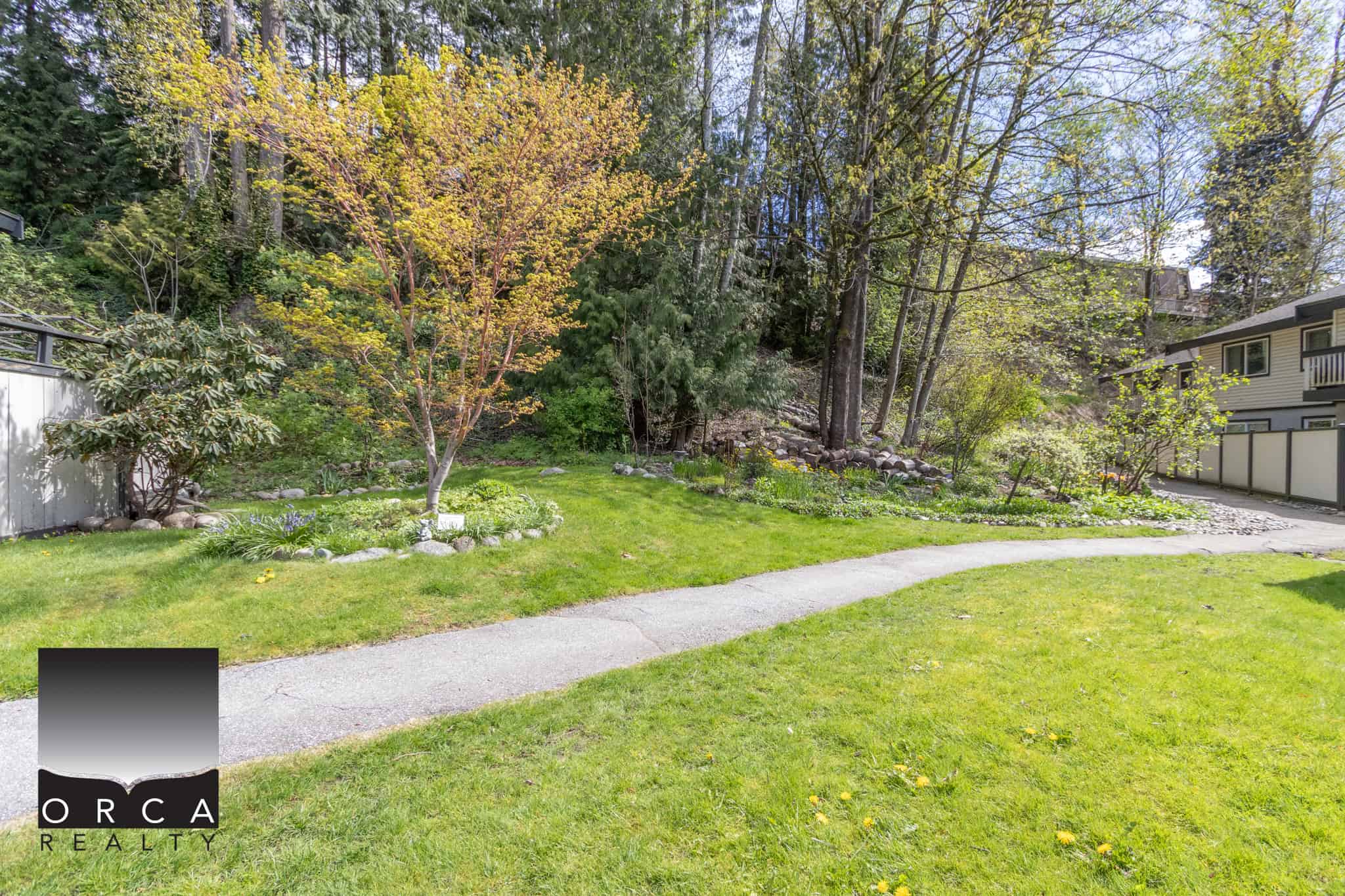 Lush green backyard with mature trees, well-maintained lawn, and natural landscaping, perfect for family outdoor activities — offered by Orca Realty Inc. in Vancouver, BC.