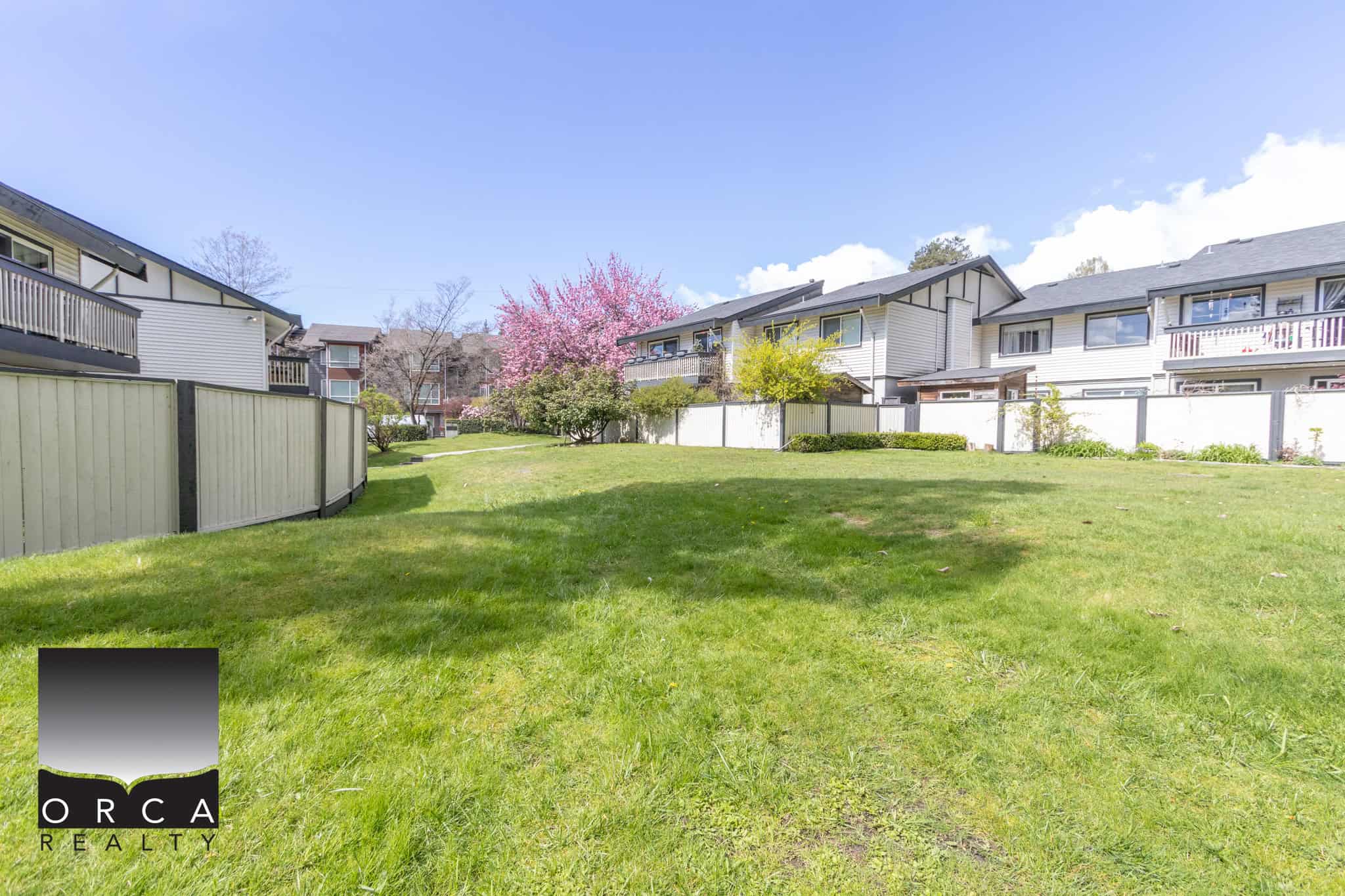 Spacious residential backyard with well-maintained green lawn, surrounded by modern townhouses and colorful blooming trees, ideal for family living and outdoor activities.