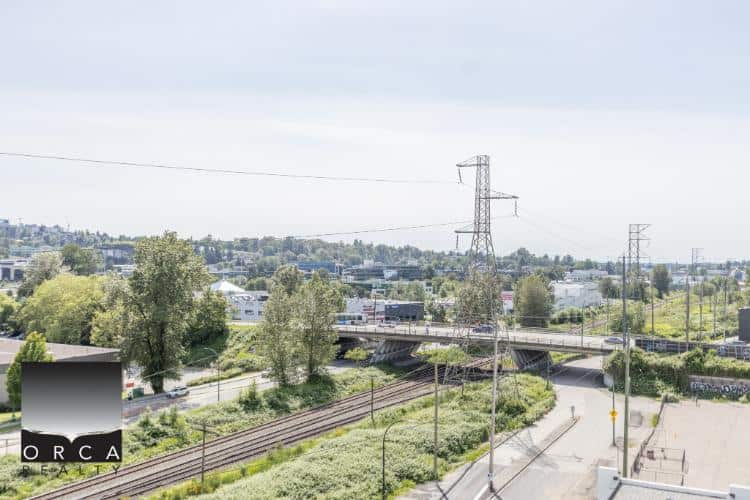 Vancouver real estate landscape featuring railway tracks, commercial buildings, and power lines with greenery, representing property opportunities in the region.