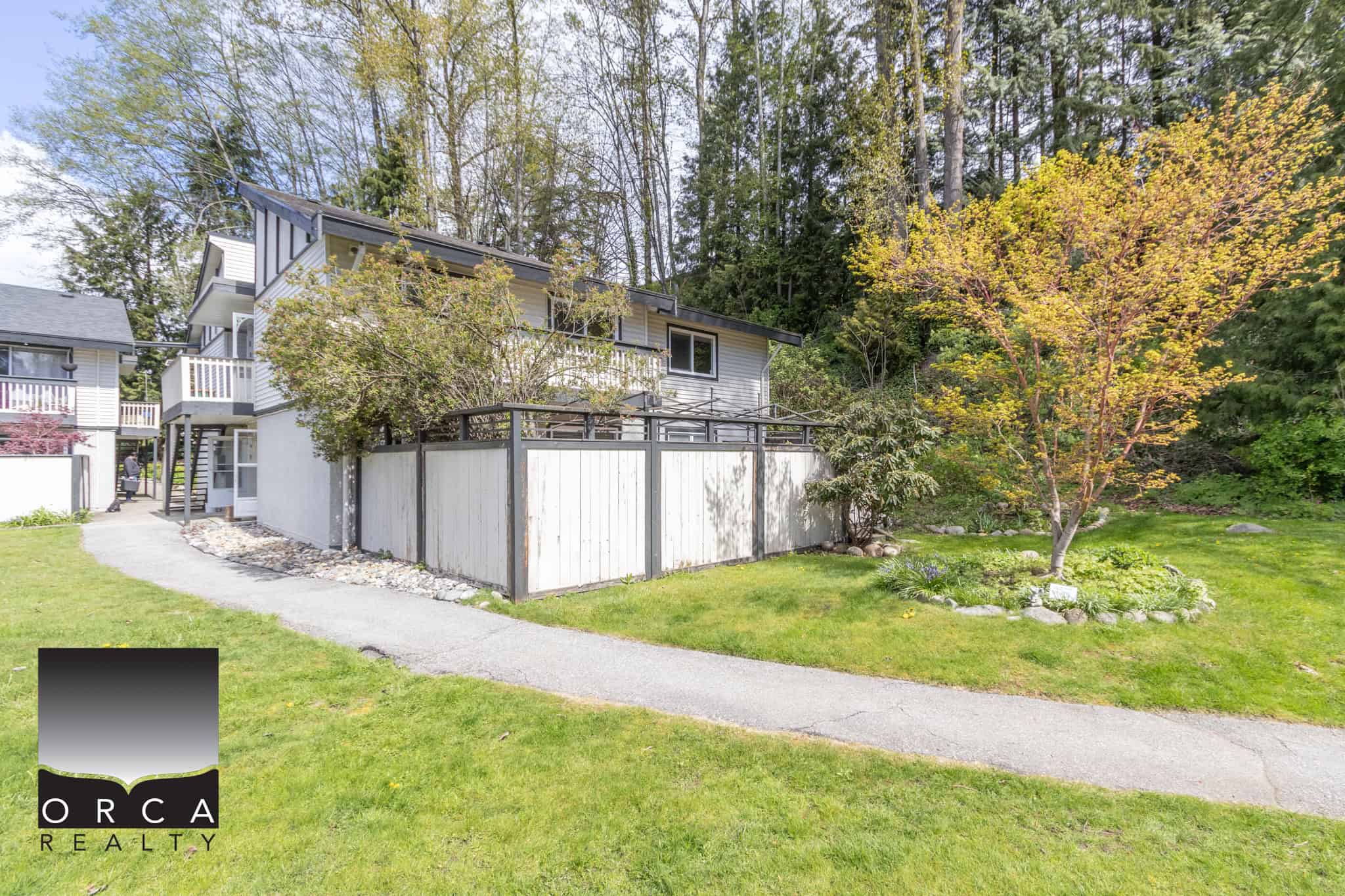 Lush green backyard with mature trees, manicured lawn, and a private fence surrounding a charming two-storey home. Ideal for outdoor living and gardening in a serene neighbourhood.
