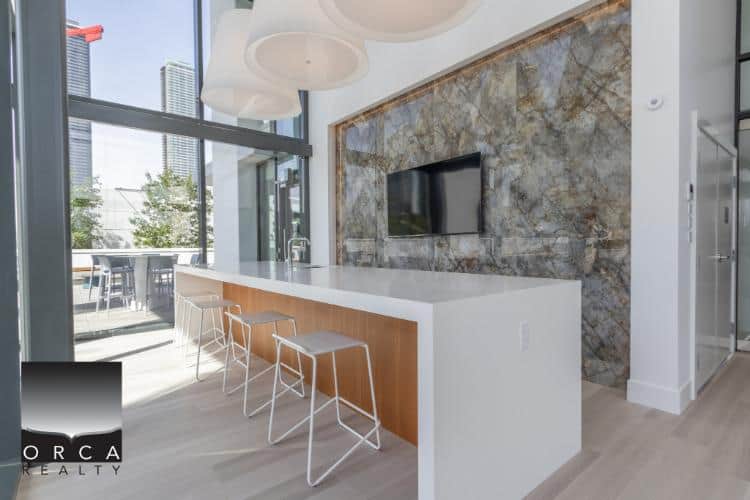Modern kitchen with sleek white countertop, contemporary bar stools, and a stone accent wall, perfect for Vancouver real estate listings.