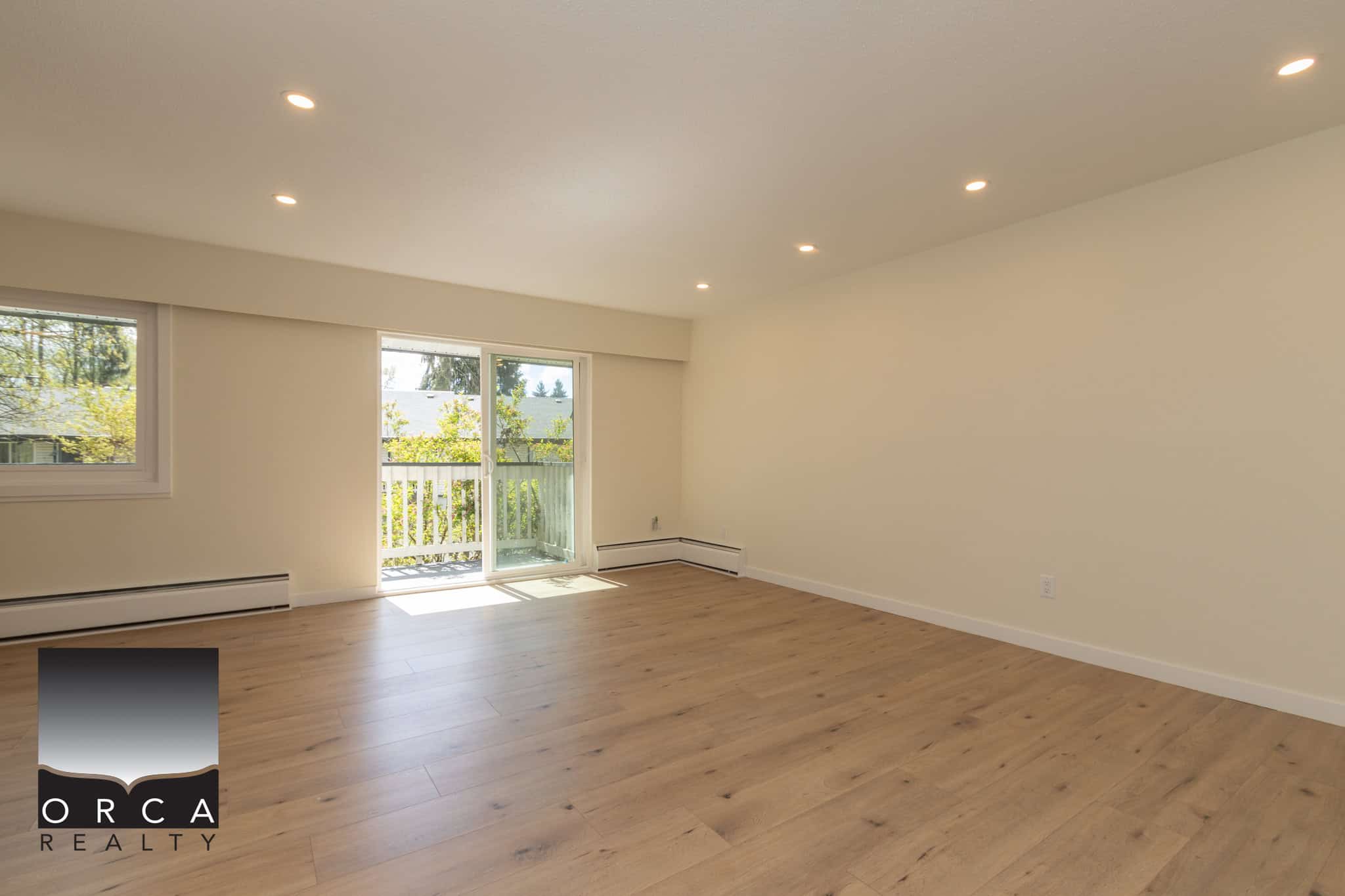 Bright and spacious living room with large windows and sliding patio door, showcasing modern interior design and natural light in a Vancouver-area home listed by Orca Realty Inc.
