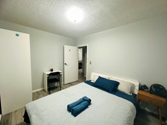 Cozy bedroom with minimalist decor, featuring a comfortable bed with blue and white linens, a small desk with chair, and essentials for a relaxing stay. Perfect for renters or short-term accommodations in BC.