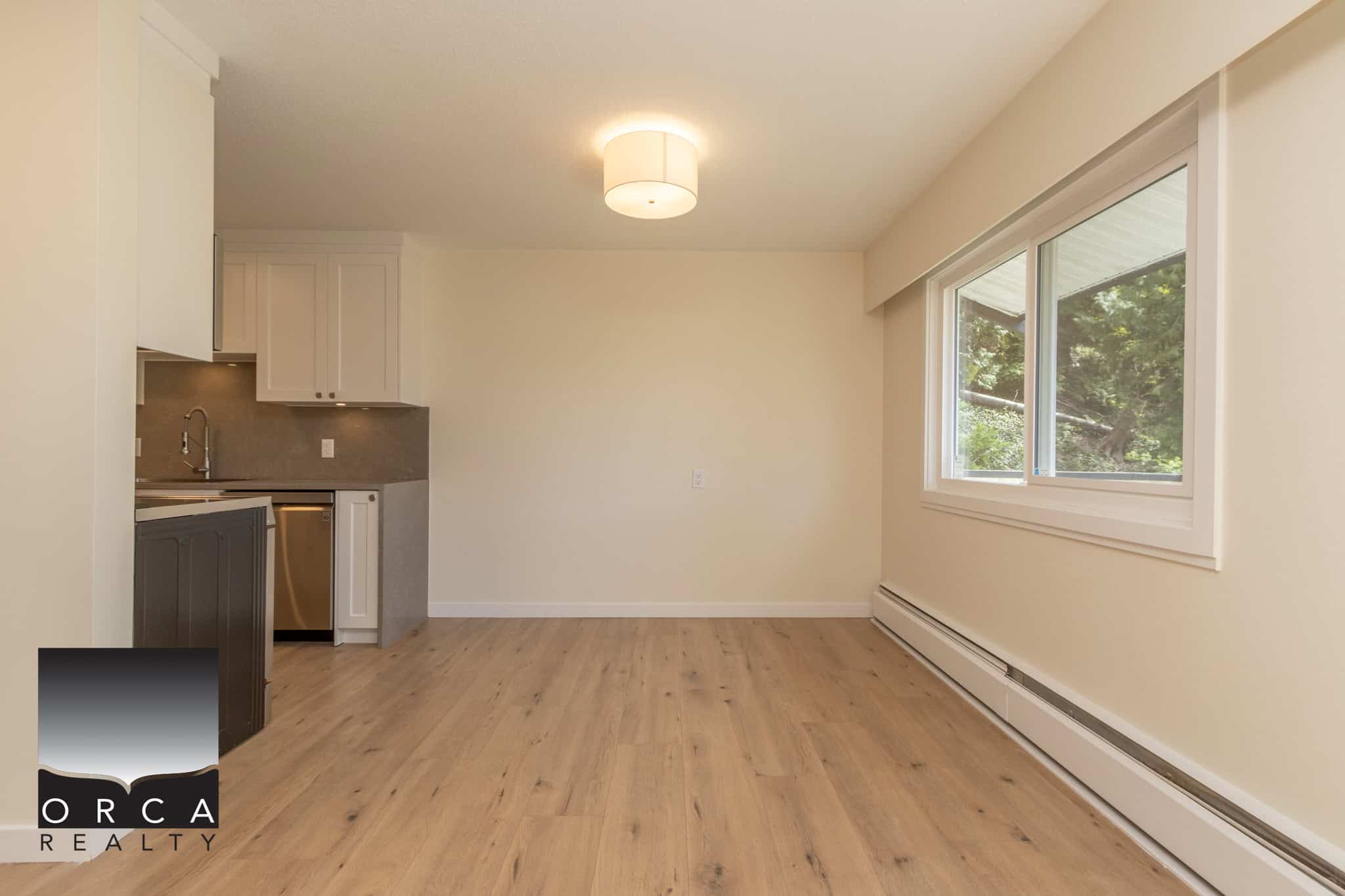 Bright open living space with large window, modern kitchen, and hardwood flooring in a Vancouver-area home listed by Orca Realty Inc.
