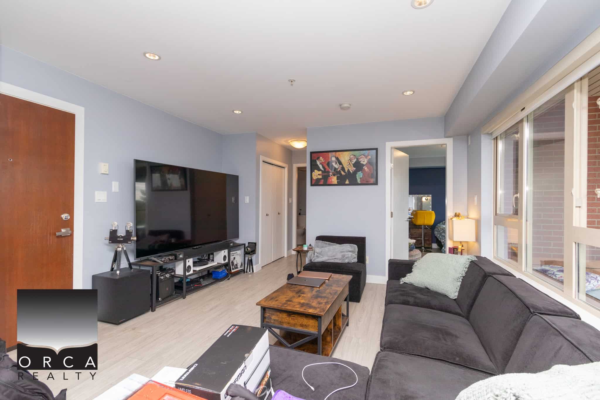 Modern living room with large windows, light hardwood floors, and contemporary furniture, showcasing a comfortable space in a Vancouver-area home listed by Orca Realty Inc.