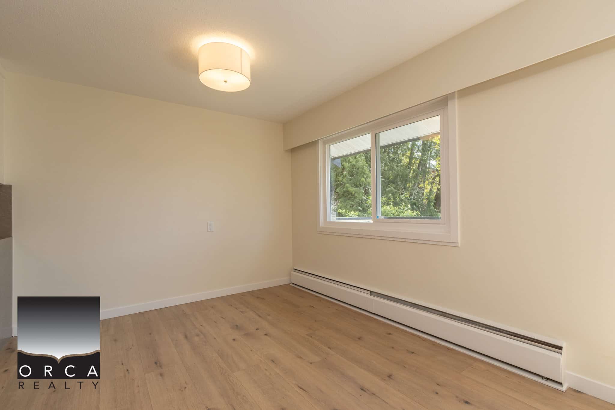 Bright and spacious living room with large window and hardwood flooring, ideal for family living or entertaining, showcasing professional real estate services offered by Orca Realty Inc.