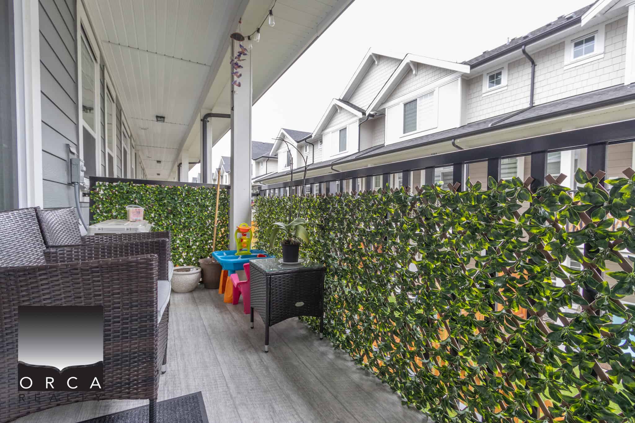 10 Balcony of a modern residential home with outdoor seating and lush greenery, overlooking neighboring townhouses, ideal for relaxation and outdoor entertaining, featured on Orca Realty Inc. website.