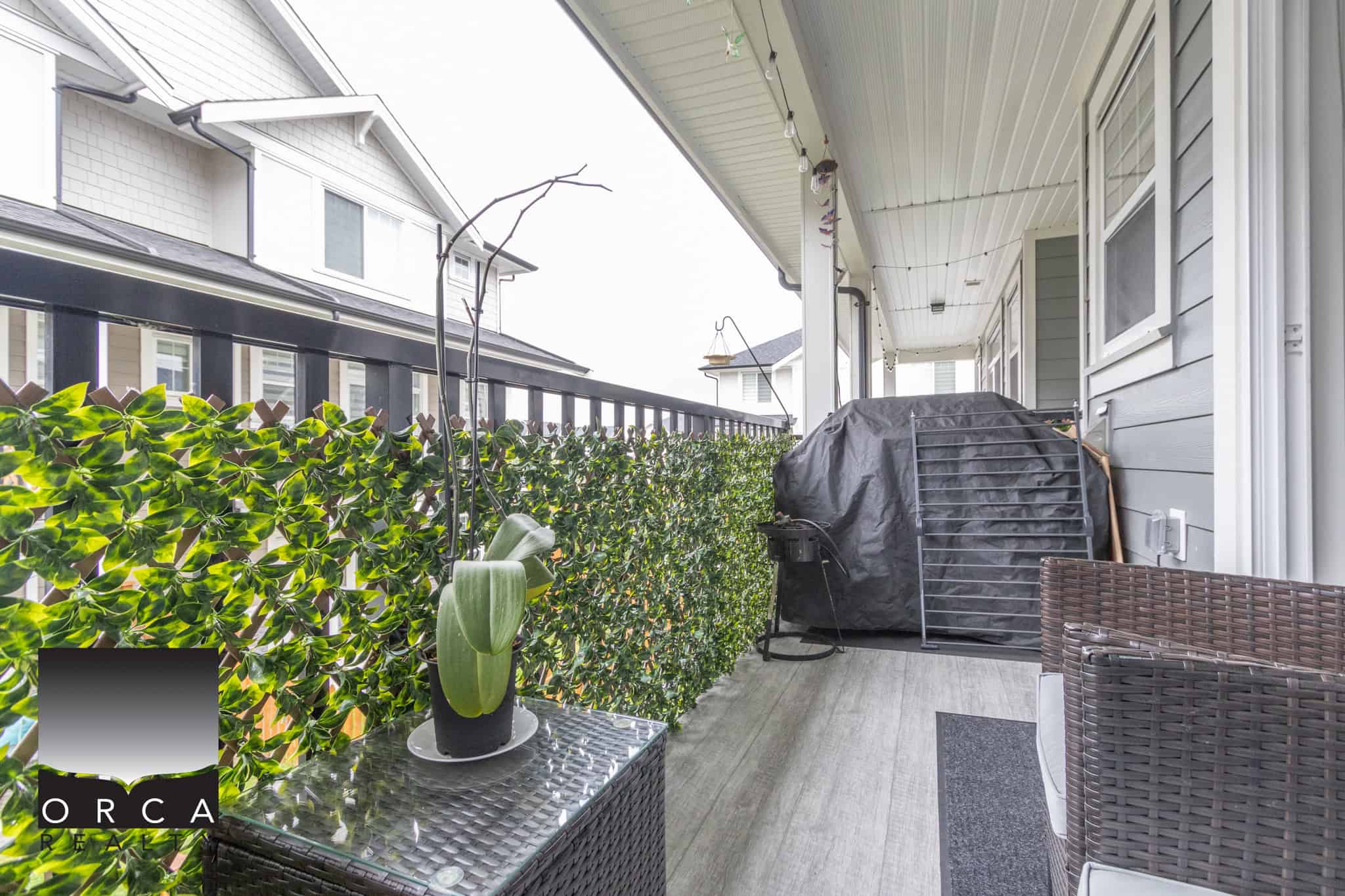 13 Cozy outdoor balcony space in a Vancouver home with privacy hedge, outdoor furniture, grill, and decorative plants, perfect for relaxing or entertaining in a peaceful neighbourhood.