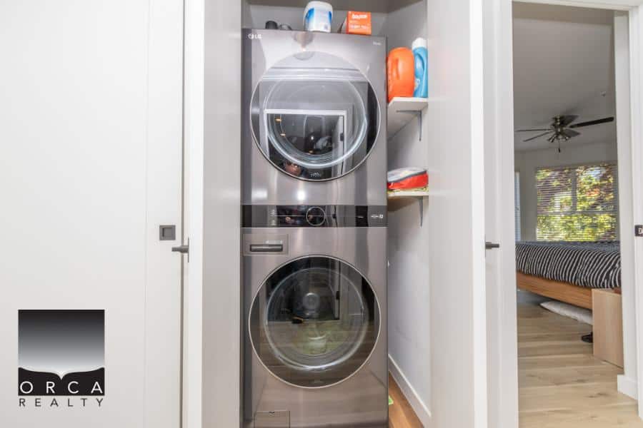 Stacked washer and dryer in a modern laundry nook, featured in a property listing by Orca Realty Inc., Vancouver Island real estate experts, showcasing functional and stylish laundry solutions.