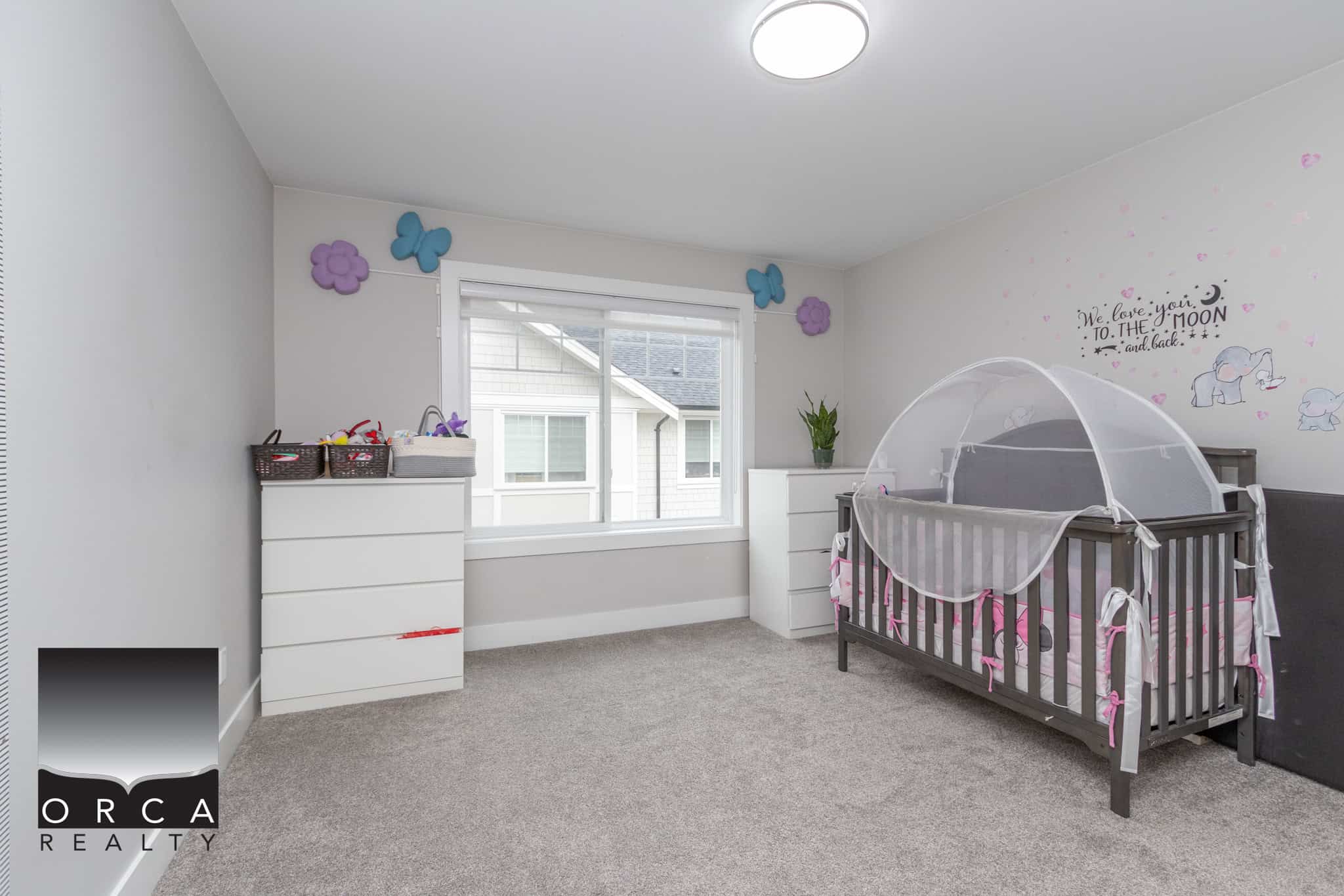 20 Bright children's bedroom with grey crib, white dressers, wall decor, and a large window, perfect for families seeking homes in Victoria, BC, featuring cozy, family-friendly interior design by Orca Realty Inc.
