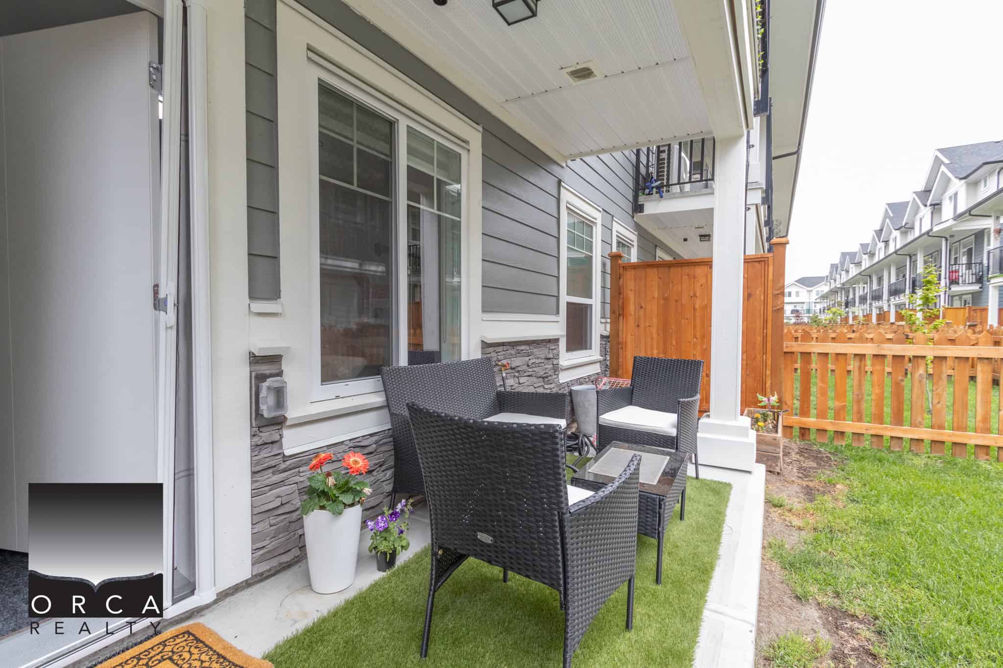 22 Cozy outdoor patio area of a modern townhouse with black wicker furniture, colorful potted flowers, and a well-maintained lawn, perfect for outdoor living.
