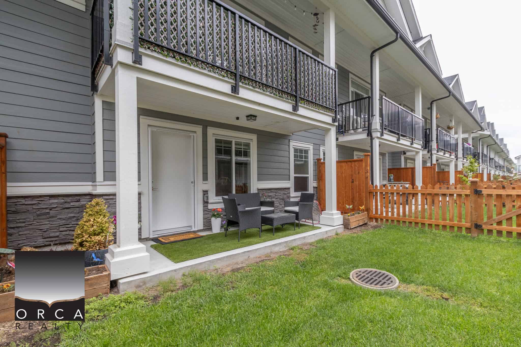 23 Modern townhouse with private backyard patio, outdoor seating area, and vibrant green lawn in a family-friendly community by Orca Realty Inc.