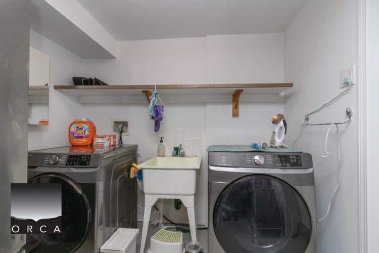 Washing machine and dryer in a modern laundry room with utility sink, shelves, and cleaning supplies. Perfect for condo, home, or rental property in Vancouver, BC.
