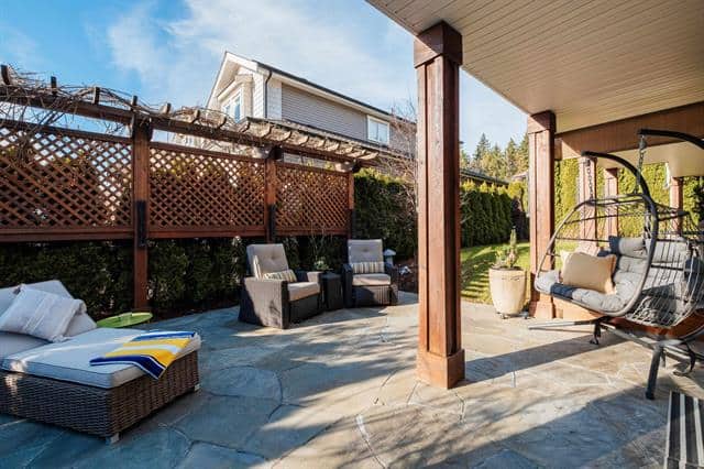 Relaxing backyard patio with outdoor seating area, wicker furniture, swing chair, and lush greenery for Vancouver homes.