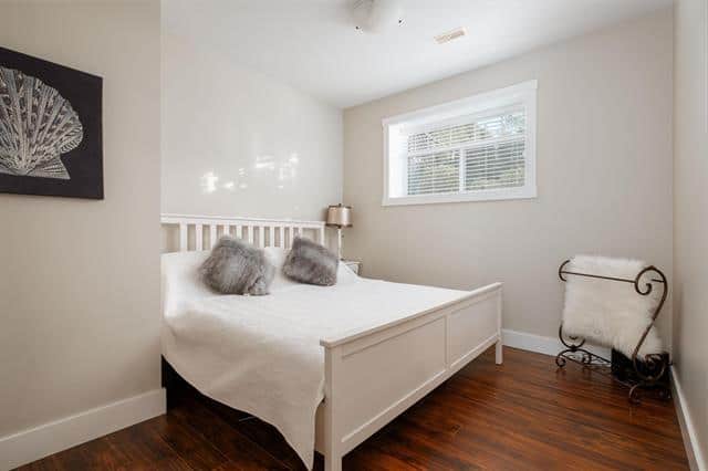 Bright and cozy bedroom with white furniture, soft pillows, and natural light from a window, showcasing ideal home staging for buyers by Orca Realty Inc.