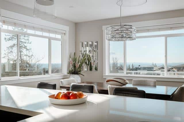 Modern bright dining room with large windows offering ocean views, stylish chandelier, and contemporary decor, perfect for coastal home living in BC.