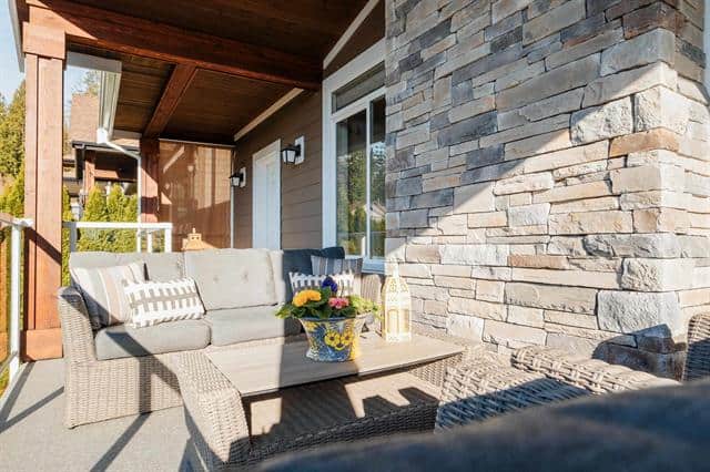Cozy outdoor patio with comfortable seating and decorative flowers, perfect for relaxing or entertaining. Modern home exterior featuring stone accents and large windows, offered by Orca Realty Inc.