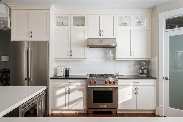 Modern white kitchen with stainless steel appliances, upper glass cabinets, and black countertops, showcasing contemporary Vancouver home design.