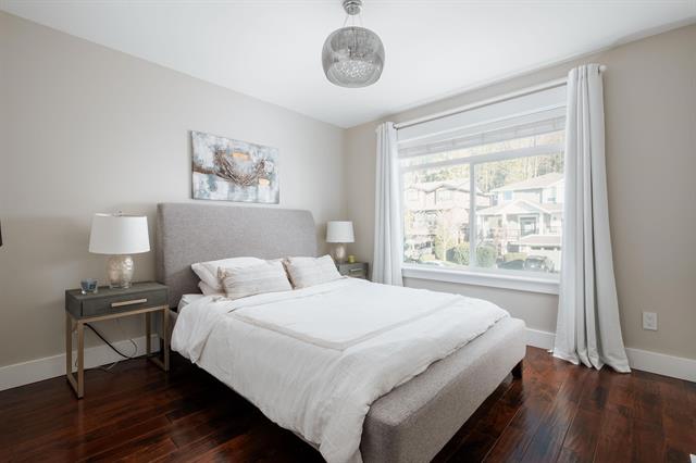 Bright modern bedroom with large window and white curtains, featuring a cozy bed with white linens, dark wood flooring, and contemporary decor, ideal for residential real estate listings in Vancouver.