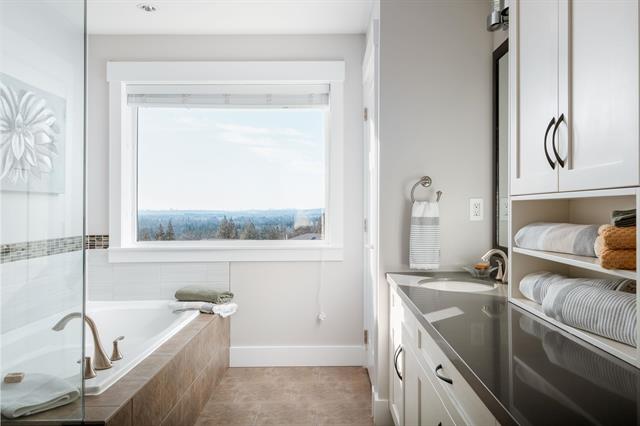 A bright bathroom with a large window offering scenic views, featuring modern cabinetry, a bathtub, and well-organized shelves, perfect for showcasing Vancouver Island real estate listings.