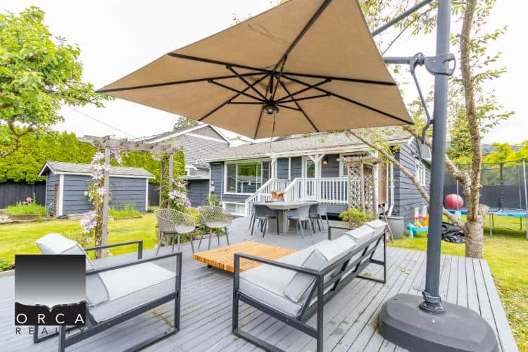 Bright outdoor patio with comfortable seating, large umbrella, and lush backyard garden, ideal for family gatherings and outdoor entertaining in Vancouver’s real estate market.