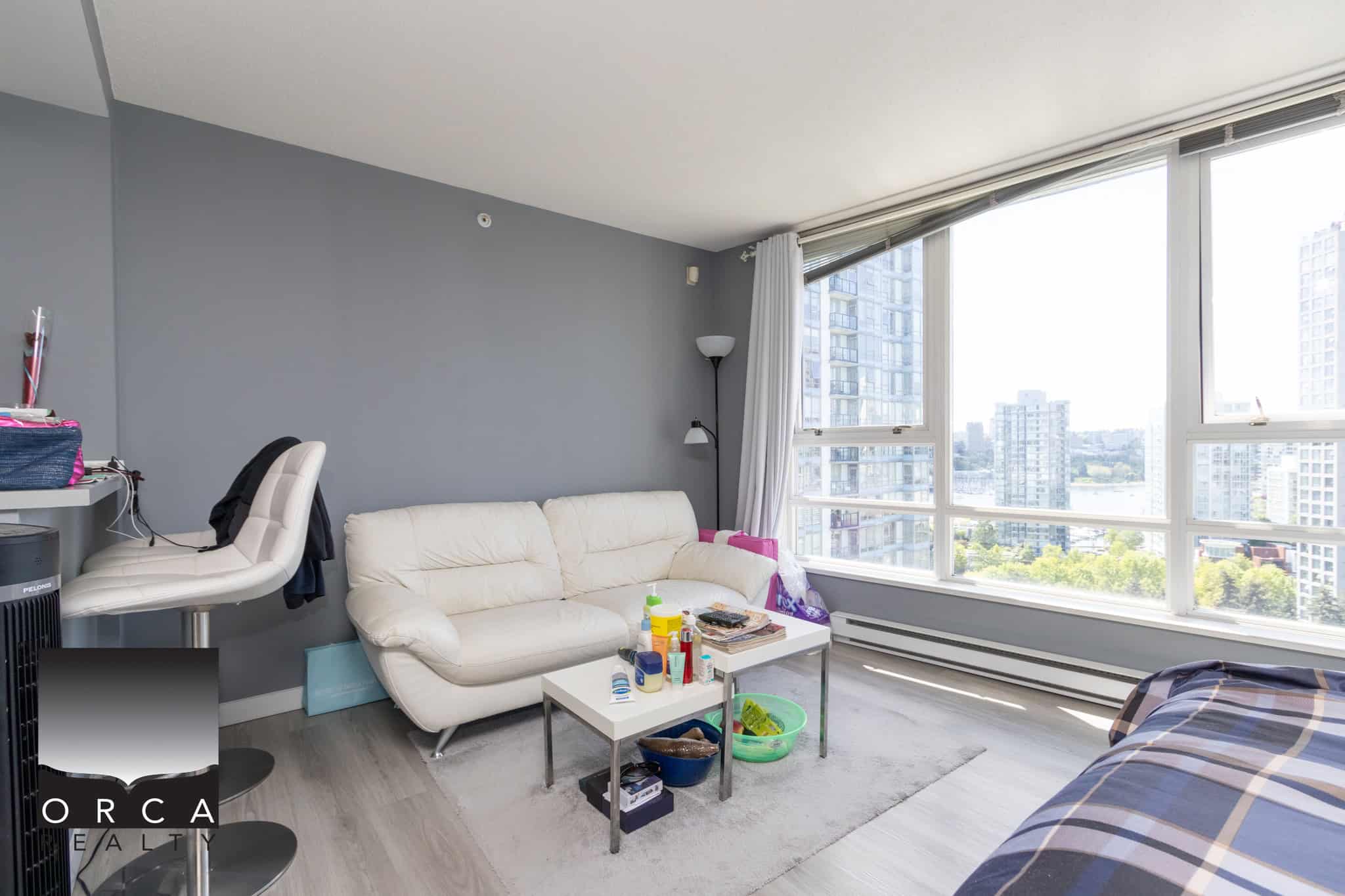 Bright modern living room with large windows showcasing city skyline in Vancouver, condo interior, minimalist decor, natural daylight, overlooking city high-rises.