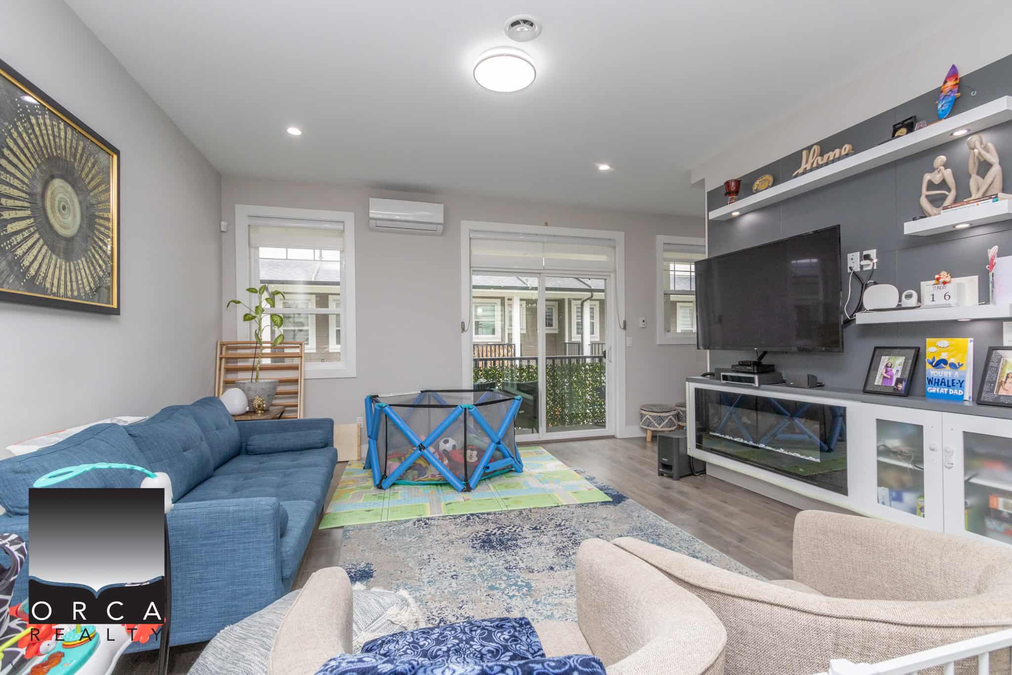3 Bright and welcoming living room at Orca Realty Inc., showcasing modern decor, a spacious layout, and family-friendly entertainment area with a TV and children's play space.