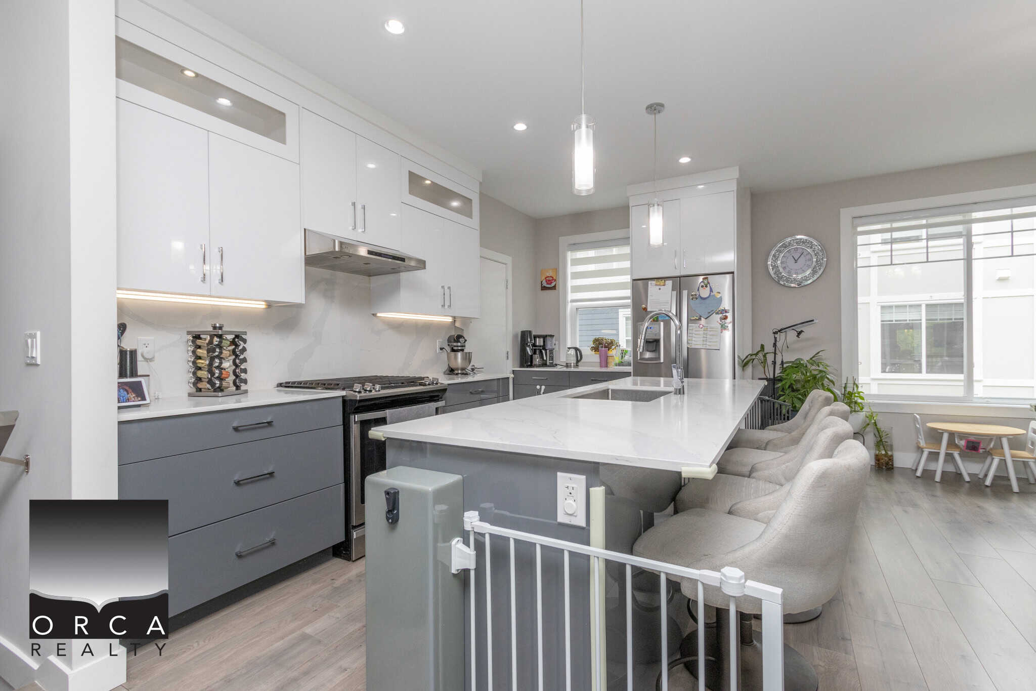 4 Modern kitchen with white and grey cabinetry, quartz countertops, stainless steel appliances, and a large island, showcasing Orca Realty Inc. properties in a contemporary home design.