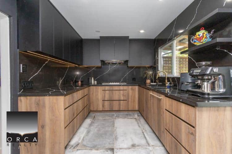 Modern kitchen with black marble countertops and wooden cabinets, featuring high-end appliances and ample natural light, ideal for real estate listings in Vancouver or surrounding BC areas.