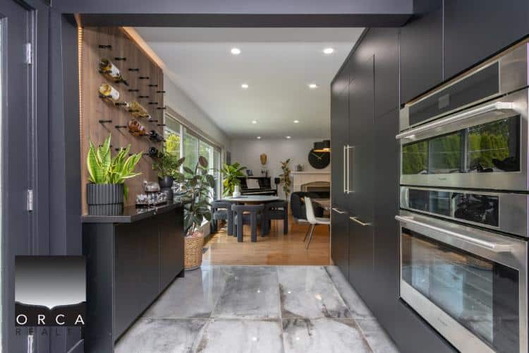 Modern open-plan kitchen and dining area with sleek black cabinetry, marble flooring, and plenty of natural light, showcasing upscale Vancouver real estate by Orca Realty Inc.