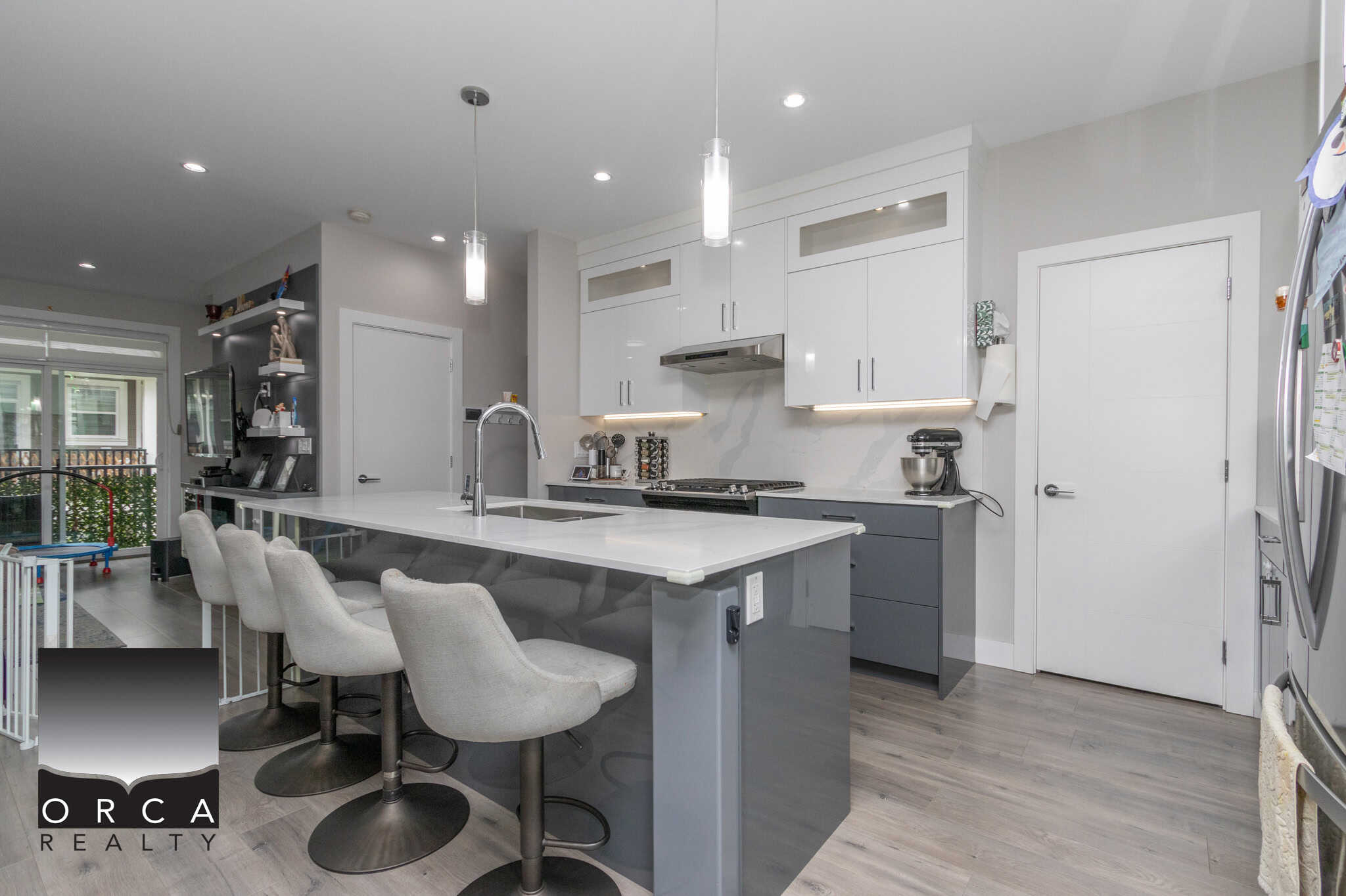 8 Modern kitchen with white and grey cabinetry, sleek appliances, and an island with seating in a contemporary home designed by Orca Realty Inc.
