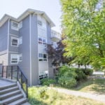 Modern grey multi-family residential building with surrounding lush greenery and mature trees, located in a vibrant neighbourhood ideal for real estate investment and property management in Victoria.