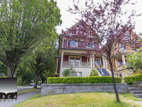 Colourful Victorian-style house surrounded by lush greenery, trees, and a well-maintained front yard, showcasing charming residential real estate listings in Vancouver by Orca Realty Inc.