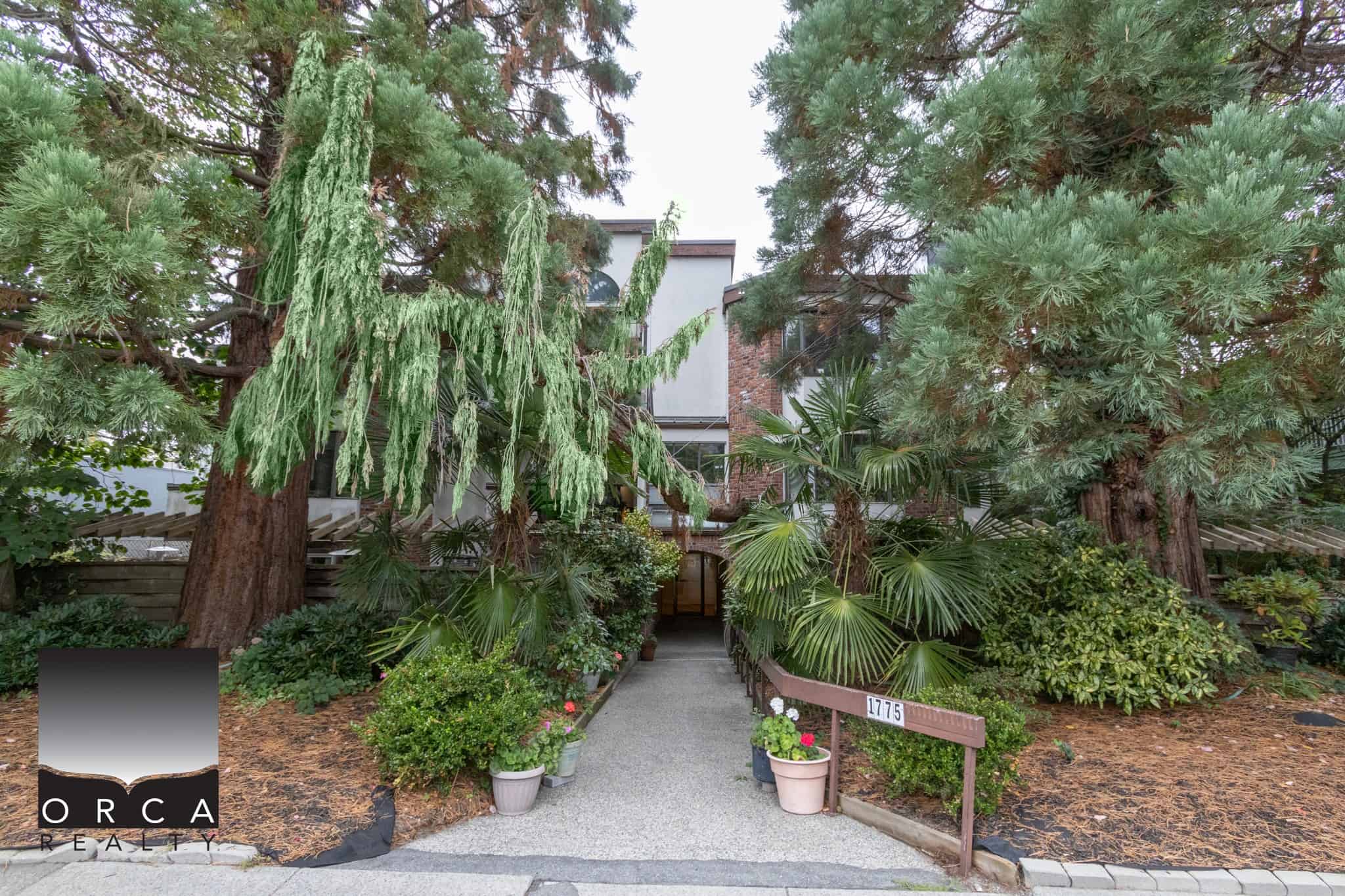 Lush greenery and tall trees surrounding the entrance of Orca Realty Inc. office building, creating a serene and inviting atmosphere for clients.
