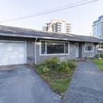 Cozy grey single-story house with attached garage, front lawn, and urban surroundings, ideal for Vancouver real estate buyers looking for a charming home with modern amenities.