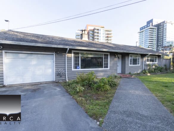Cozy grey single-story house with attached garage, front lawn, and urban surroundings, ideal for Vancouver real estate buyers looking for a charming home with modern amenities.