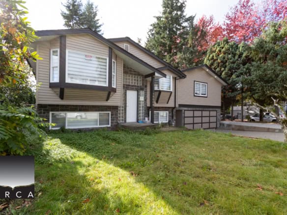Spacious split-level family home in Vancouver with large windows, green lawn, mature trees, and a garage, ideal for families and homebuyers seeking comfort and style in a vibrant neighbourhood.