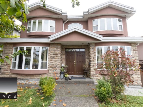 Spacious Vancouver home exterior with a stone and stucco facade, lush landscaping, and a welcoming front door, showcasing Orca Realty Inc.'s expert real estate services in BC.