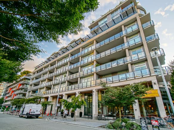 Contemporary multi-story residential building with glass balconies and retail shops on the ground floor in a vibrant urban setting.