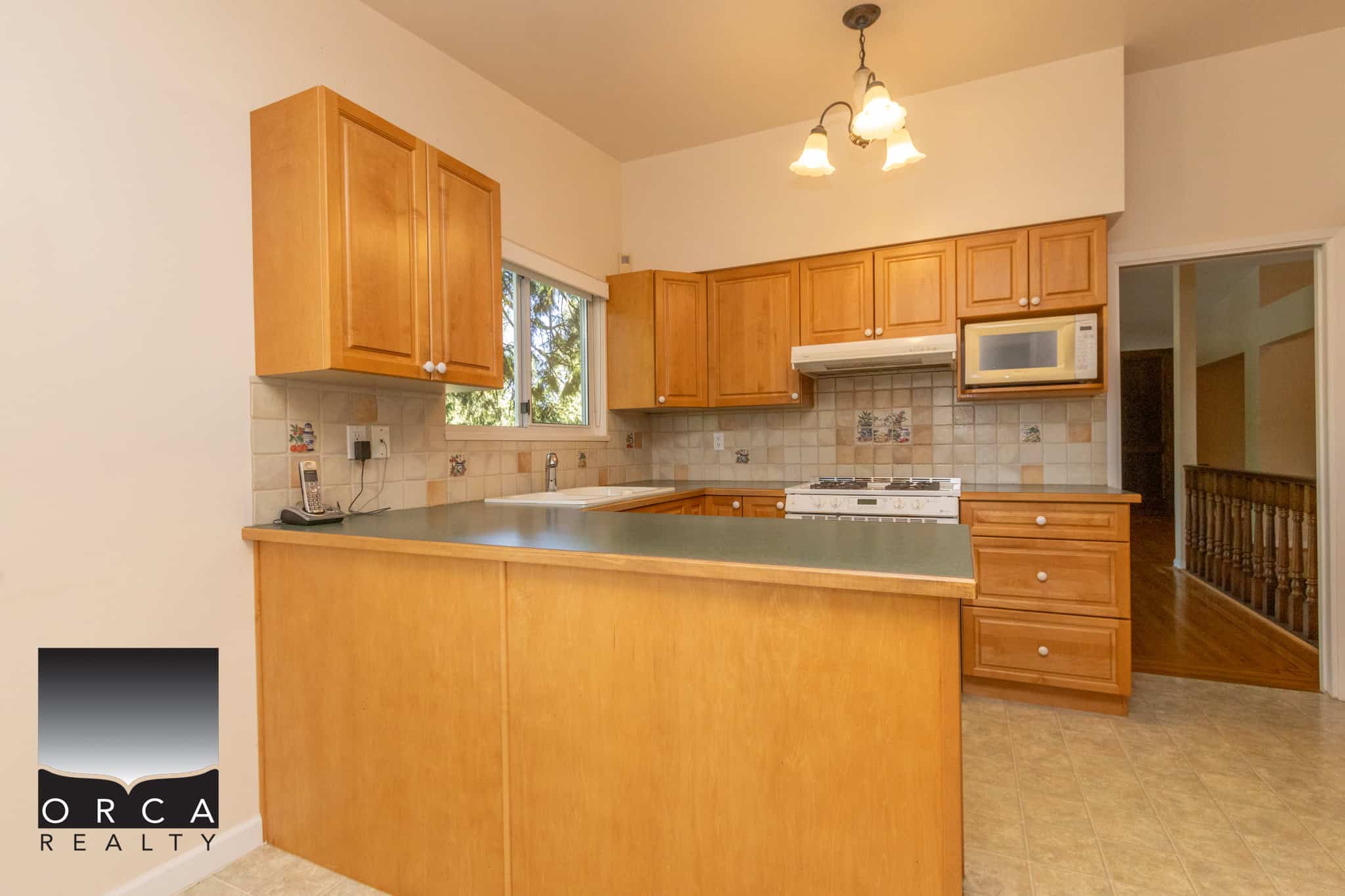 Bright kitchen with wooden cabinets, tile backsplash, and modern appliances including microwave, stove, and sink, in a cozy home setting ideal for families and individuals.