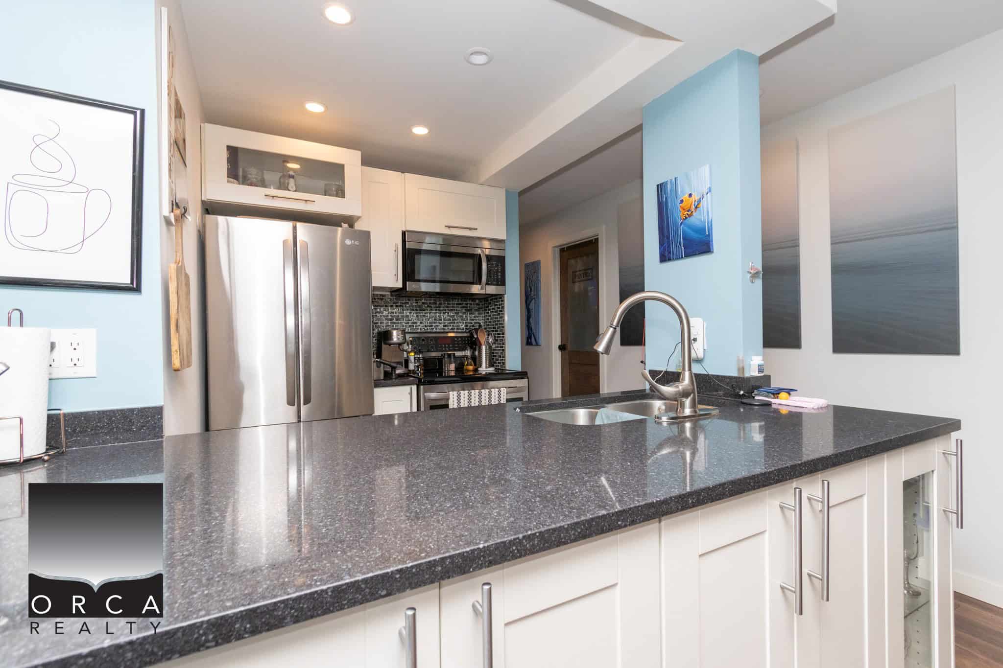 Stainless steel refrigerator and modern kitchen appliances in a contemporary kitchen, featuring a black granite countertop, white cabinetry, and ocean-inspired artwork, ideal for Vancouver Island homes.