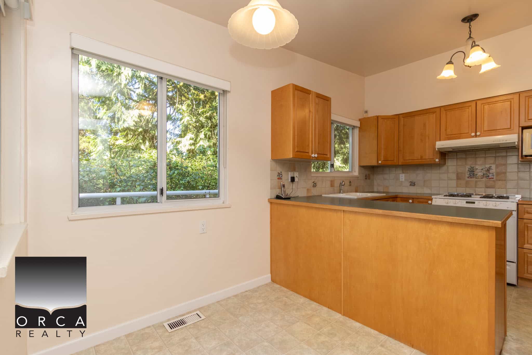 Bright kitchen with natural light from large window, featuring wooden cabinetry, neutral tile backsplash, and functional layout, ideal for modern Canadian homes.